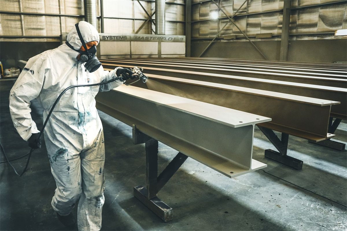 Painter in a white hooded coverall and respirator spraying steel beams