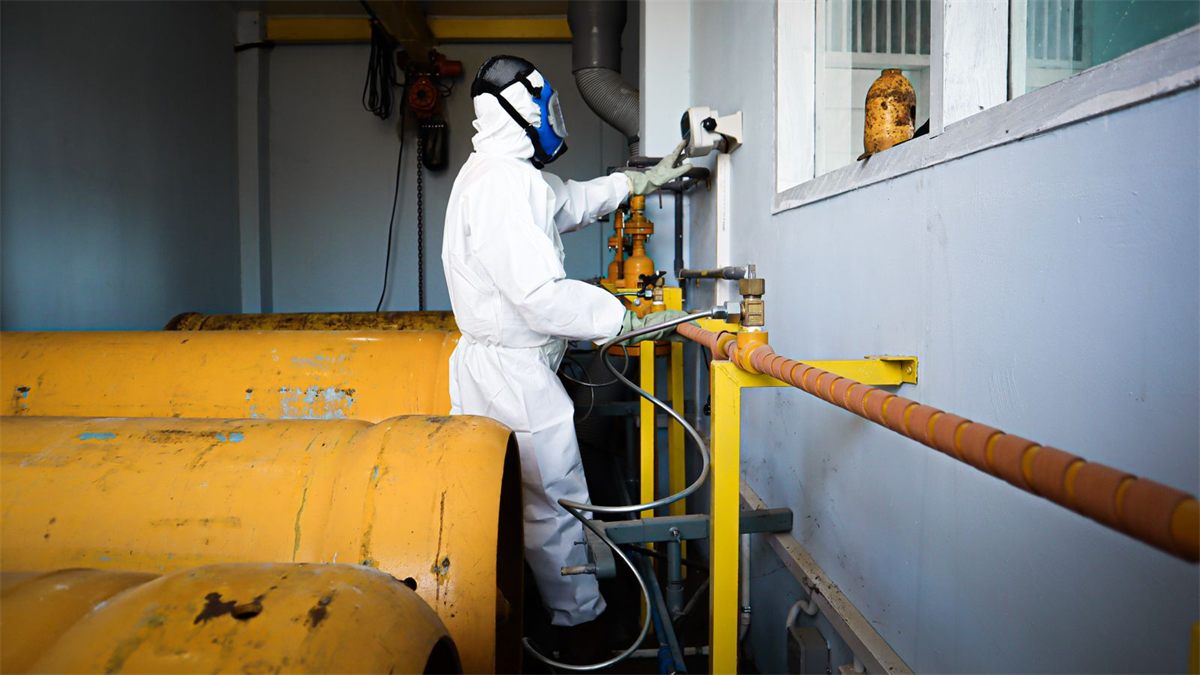 Worker in a white hooded coverall and full-face respirator beside gas cylinders
