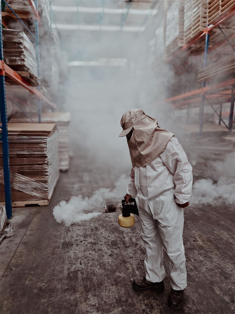 Pest control technician in a white coverall fogging a warehouse aisle